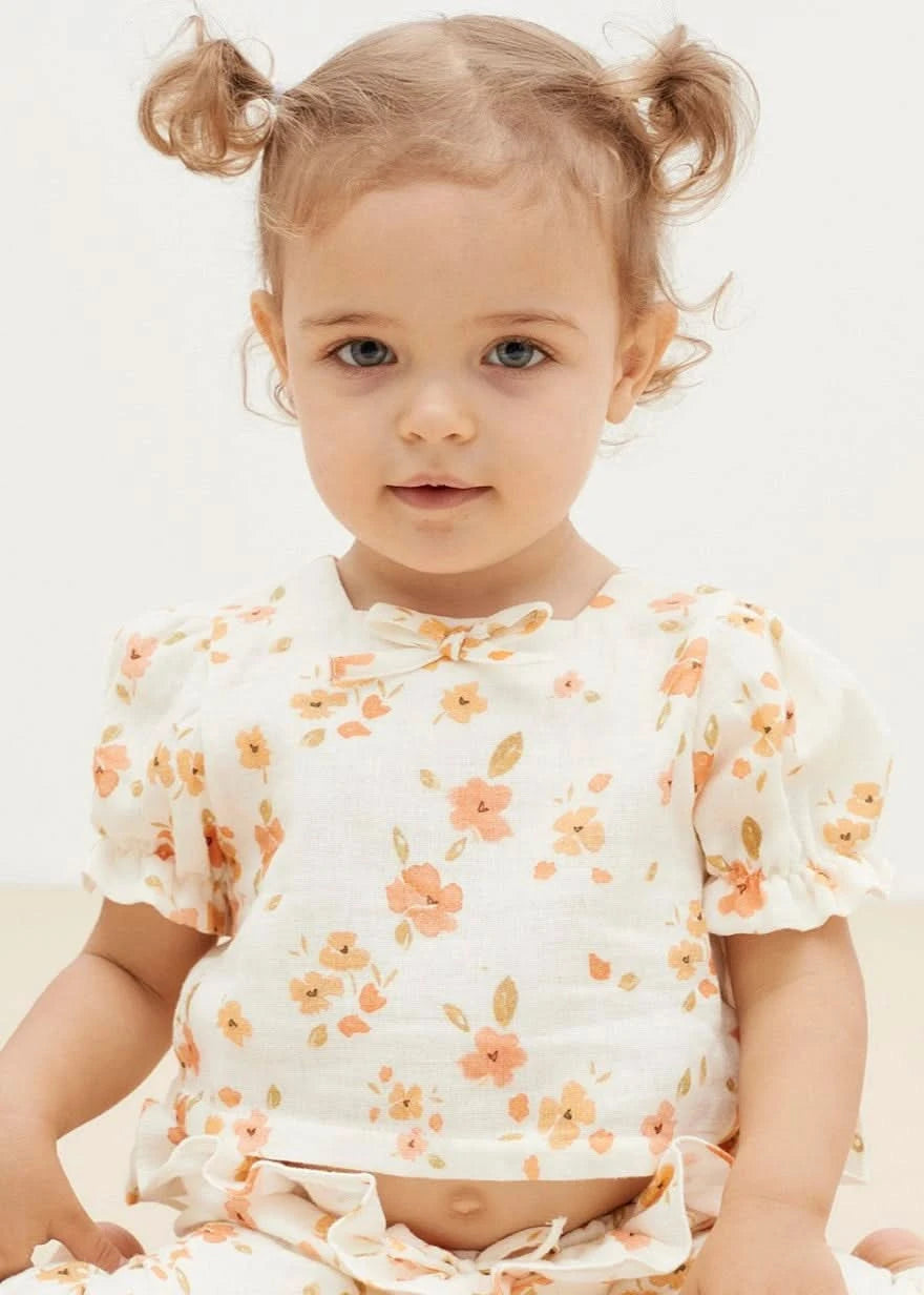 White baby blouse with floral print, puff sleeves, square neckline, and bowtie detail.