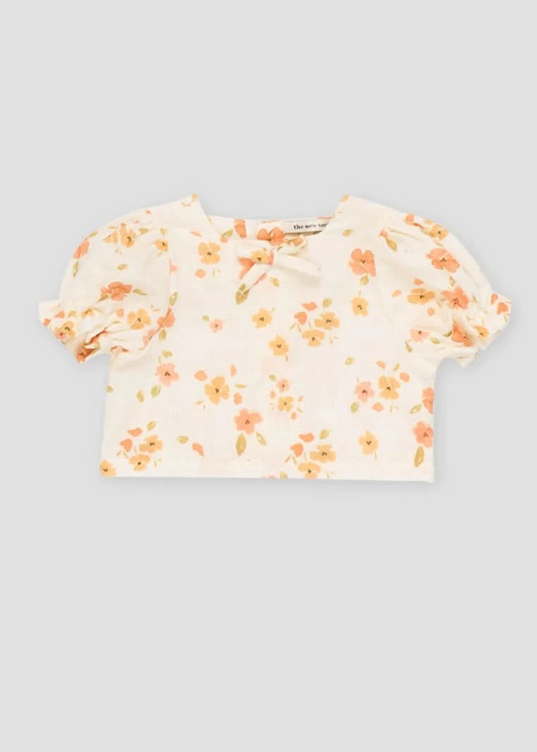 White baby blouse with floral print, puff sleeves, square neckline, and bowtie detail.